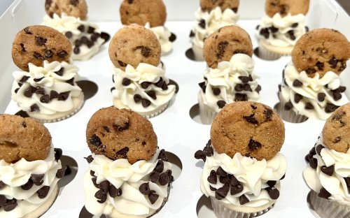 A tray of mini cupcakes topped with swirls of frosting, chocolate chips, and a cookie on each.