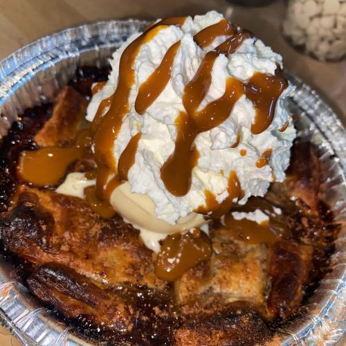A warm dessert in a foil dish topped with whipped cream, caramel sauce, and a scoop of ice cream.