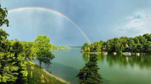 A serene lake scene with a vibrant rainbow arching over lush green trees and calm waters.