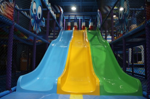 Colorful slides in a play area, featuring blue, yellow, and green slides with a playful octopus decoration in the background.