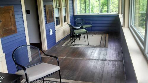A spacious porch with two chairs, a patterned rug, and large windows overlooking greenery.