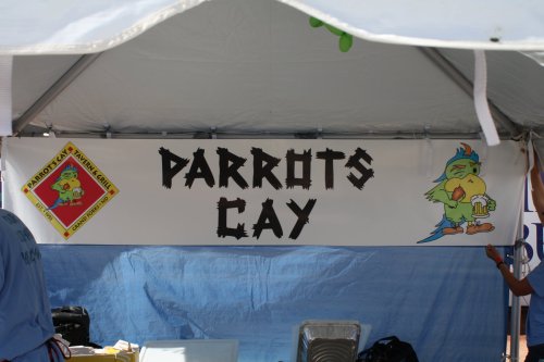A banner reading "Parrots Cay" with colorful parrot illustrations, displayed at a booth under a tent.