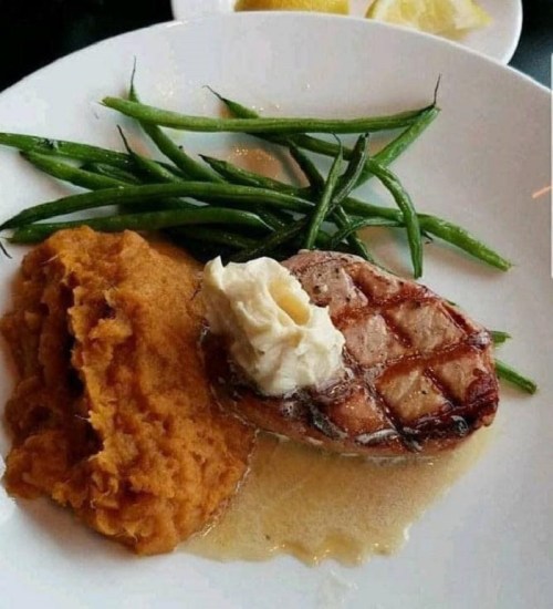 A plate featuring grilled meat with a buttery topping, sweet potato mash, and green beans on the side.