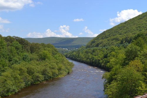 A winding river flows through lush green hills under a blue sky with fluffy clouds.