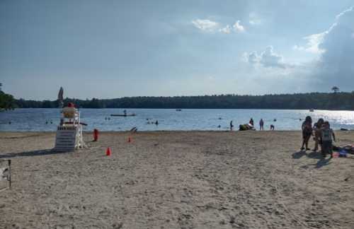 A sandy beach with a lifeguard tower, people swimming in the lake, and a cloudy sky in the background.