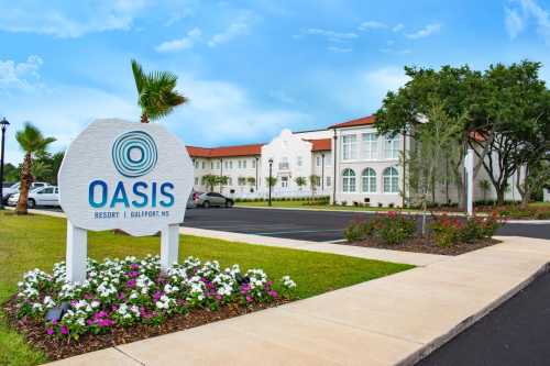 Sign for Oasis Resort in Gulfport, MS, with a landscaped entrance and a blue sky in the background.