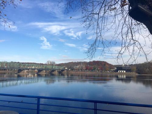 A serene river view with a bridge, trees, and colorful autumn foliage under a clear blue sky.