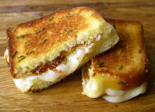 A golden-brown grilled cheese sandwich with melted cheese and a hint of herbs, cut in half on a wooden surface.