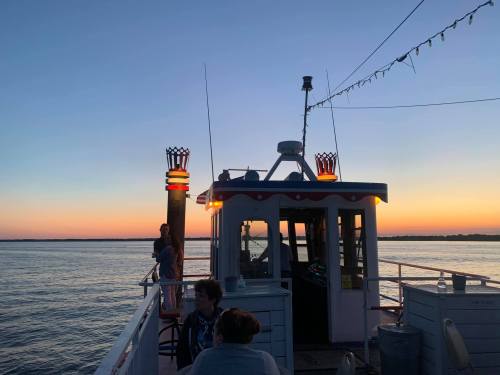 A boat at sunset, with warm lights glowing and people enjoying the view on a calm waterway.
