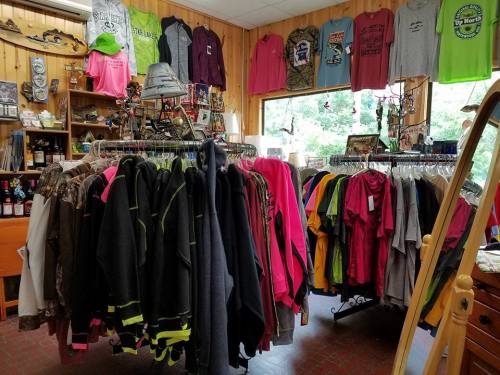 A clothing store interior featuring racks of colorful shirts, including camo and bright neon options, with various accessories.