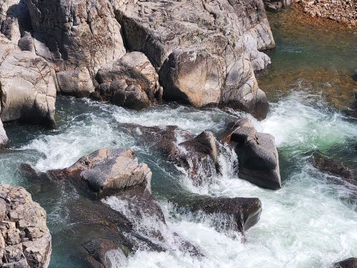 Rushing water flows over rocky terrain, creating white foam and clear pools in a natural landscape.