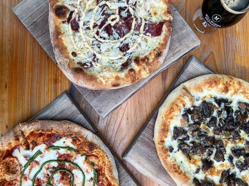 Three pizzas on wooden boards: one with white sauce and meat, one with pepperoni and cheese, and one with beef and herbs.