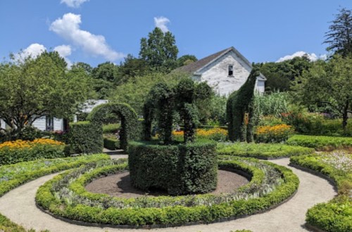 A beautifully landscaped garden featuring topiary shapes, colorful flowers, and a clear blue sky in the background.