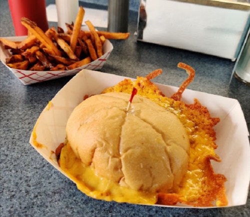 A cheesy burger with a red toothpick, served with a side of crispy sweet potato fries in a basket.