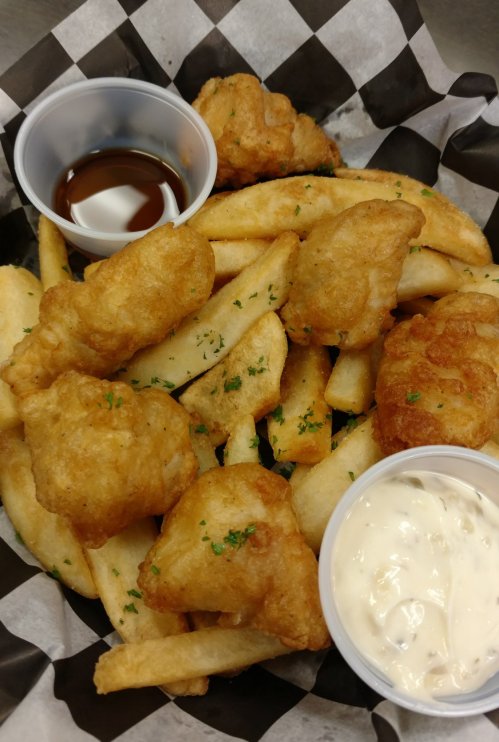 A basket of golden fried fish pieces and crispy French fries, served with dipping sauces.