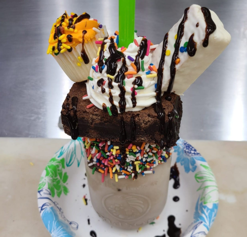 A decadent milkshake topped with whipped cream, chocolate drizzle, sprinkles, a brownie, and two mini cupcakes.