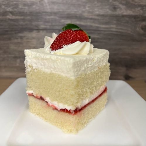 A slice of vanilla cake layered with strawberry filling, topped with whipped cream and a fresh strawberry.