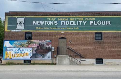 Mural on a brick building featuring "Newton's Fidelity Flour" and signs for a visitor center and a museum.