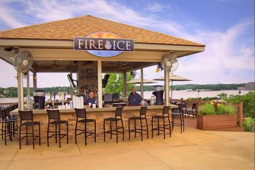 A lakeside bar named "Fire & Ice" with two bartenders, outdoor seating, and a scenic view of the water.