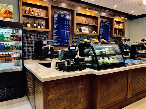 A modern café counter with a display case of pastries, coffee machines, and a menu board in a stylish interior.