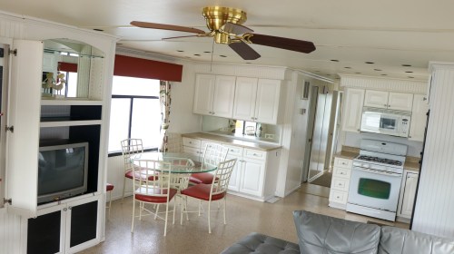 Bright, modern kitchen and dining area with white cabinetry, a glass table, and a ceiling fan. Cozy living space visible.