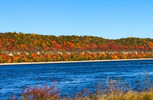 A vibrant autumn landscape with colorful trees along a river under a clear blue sky.