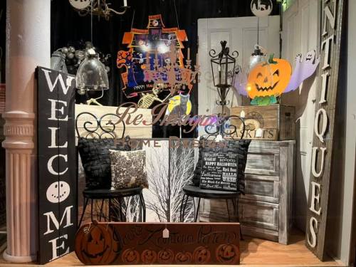 A cozy display featuring Halloween decorations, antique furniture, and welcoming signs in a charming shop setting.