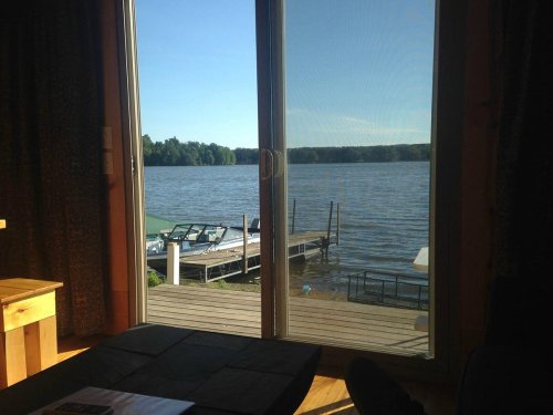 View of a serene lake from a cabin, with a wooden dock and boats visible under a clear blue sky.