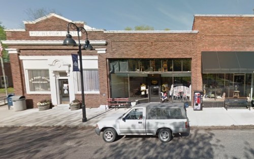 A street view of a small town with a post office and a café, featuring a parked SUV in front.