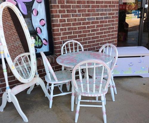 A colorful outdoor seating set with a round table, four chairs, a mirror, and a decorative storage chest against a brick wall.