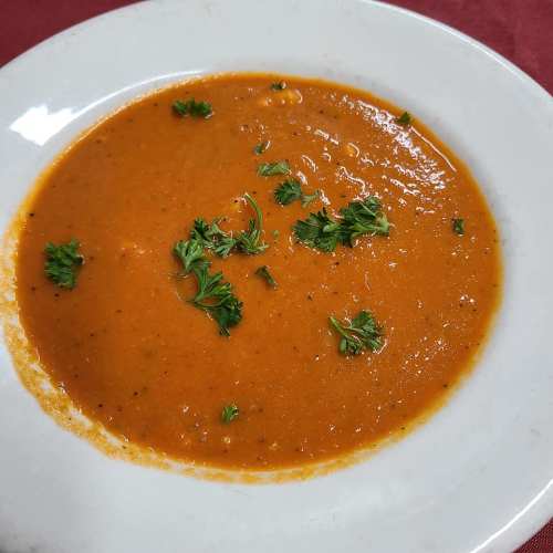 A bowl of smooth tomato soup garnished with fresh parsley on a white plate.