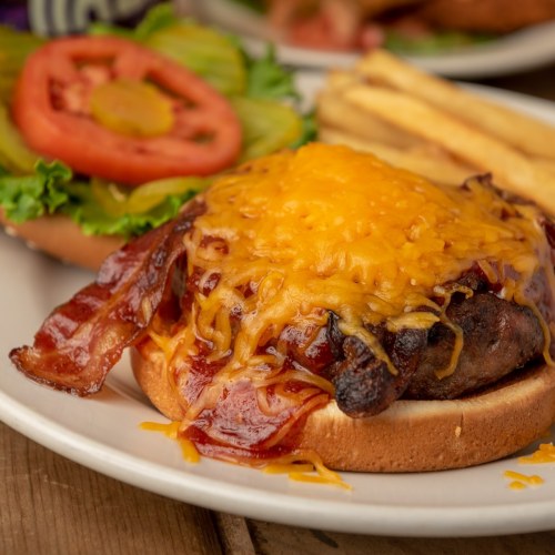 A juicy burger topped with melted cheese, crispy bacon, and fresh lettuce and tomato, served on a toasted bun.