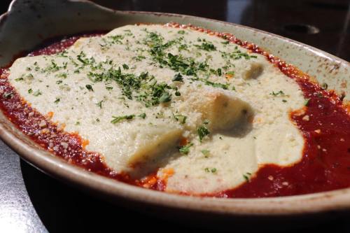 A dish of gnocchi topped with creamy sauce and sprinkled with herbs, served in a shallow dish with red sauce.