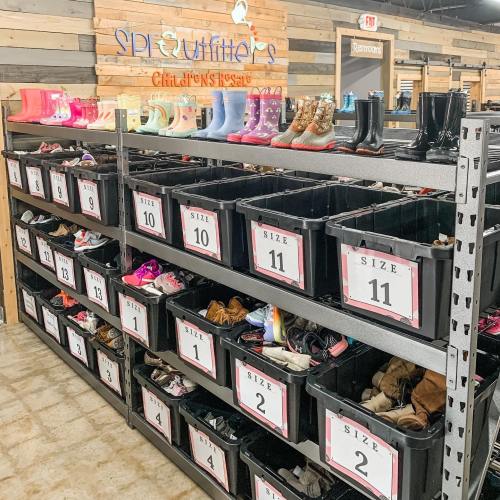 A display of children's shoes organized by size in bins, with colorful boots on top shelves in a store setting.