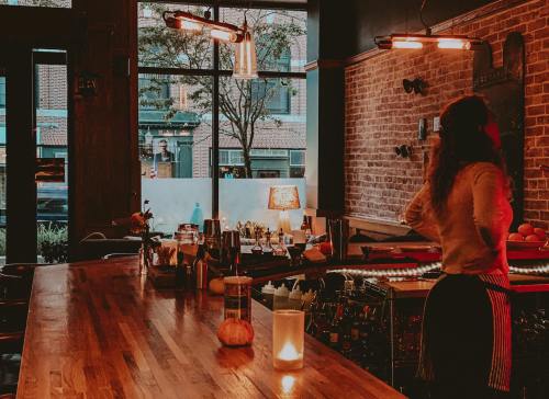 A cozy bar scene with a wooden counter, shelves of drinks, and a bartender preparing cocktails in warm lighting.