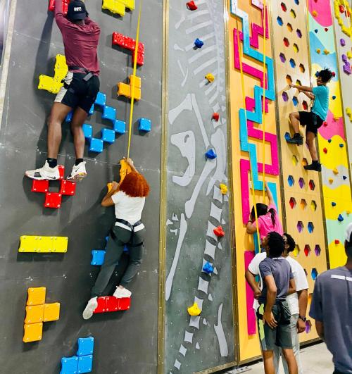 A group of people climbing a colorful indoor rock wall with various climbing holds and routes.