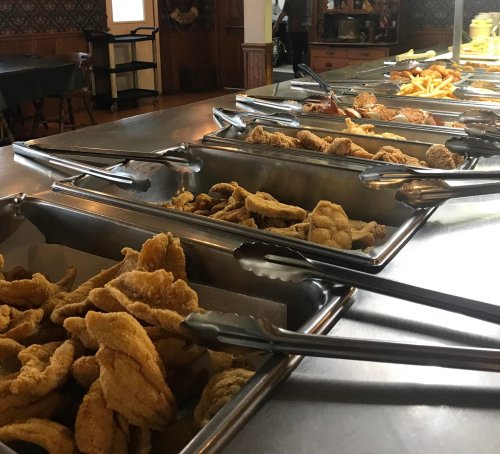 A buffet table with various trays of fried food, including fish and chicken, ready for serving.