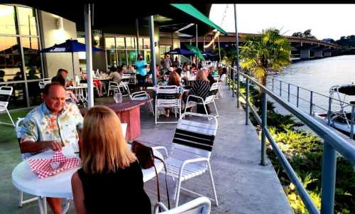 Outdoor dining area by the water, with people enjoying meals at tables under umbrellas.