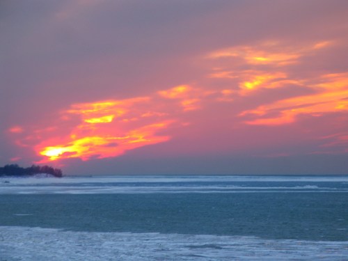 A vibrant sunset over a calm sea, with hues of orange, pink, and purple reflecting on the water's surface.