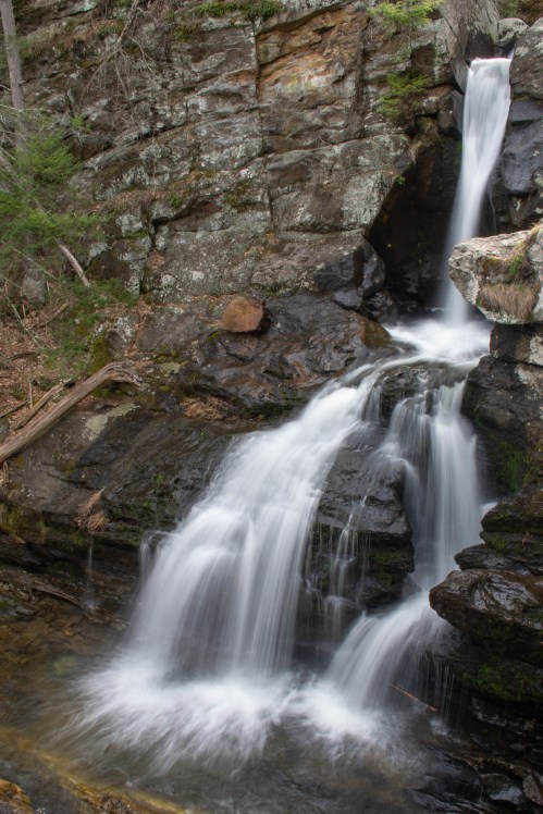 A serene waterfall cascading over rocky terrain, surrounded by lush greenery and natural stone formations.
