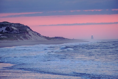 A serene beach at sunset, with gentle waves and a distant lighthouse silhouetted against a colorful sky.