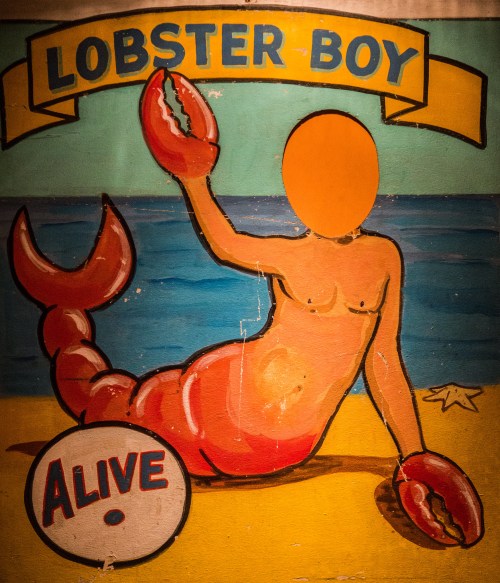 Colorful mural of a lobster-themed character on a beach, holding a lobster, with an empty face area.
