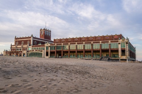 Historic beachfront building with large windows, set against a sandy shore and cloudy sky.