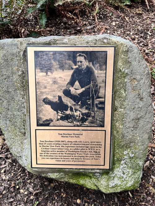 A plaque honoring Tom Dechene, featuring a photo of him sitting by a fire, surrounded by nature.