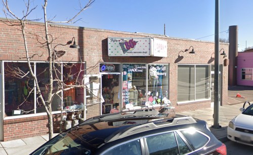 A colorful storefront with a sign reading "Totally Awesome Shop!" and an "Open" sign, featuring large windows and a parked car.