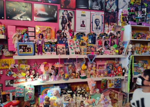 A colorful display of vintage toys and collectibles on shelves against a pink wall, featuring dolls and memorabilia.