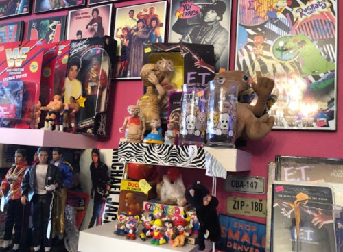 A colorful display of vintage toys, including action figures, plush toys, and retro posters on a pink wall.