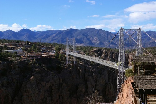 A suspension bridge spans a canyon, with mountains in the background and a small town nestled below.