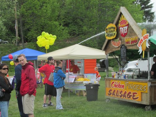 A food festival scene with vendors selling burgers, fries, and hot dogs, colorful balloons, and people enjoying the event.