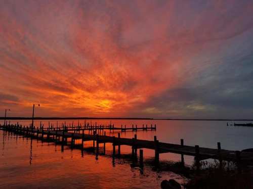 A vibrant sunset over a calm lake, with a wooden pier extending into the water and colorful clouds in the sky.